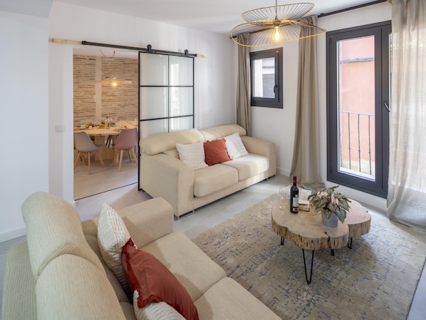 A modern living room with a sofa, a dining area, and a sliding glass door to the outside.