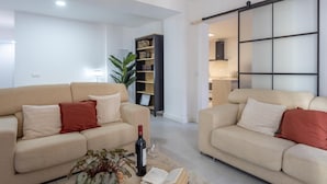 A modern living room with two beige sofas, a coffee table with a book and a bottle, and a bookshelf. - CASA BOUTIQUE SAN JUAN (LOGROÑO)