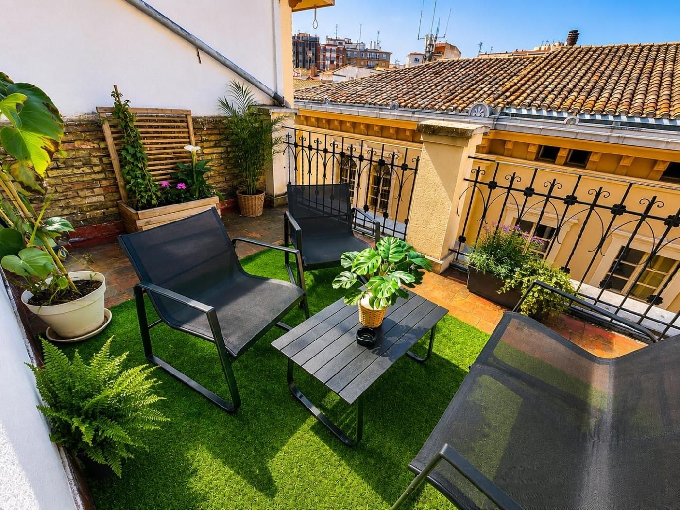 A rooftop patio with two chairs, a table, and potted plants.