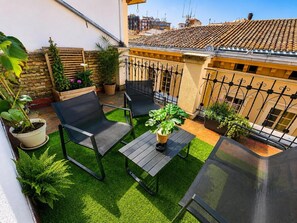 Um terraço no telhado com duas cadeiras, uma mesa e plantas em vasos.