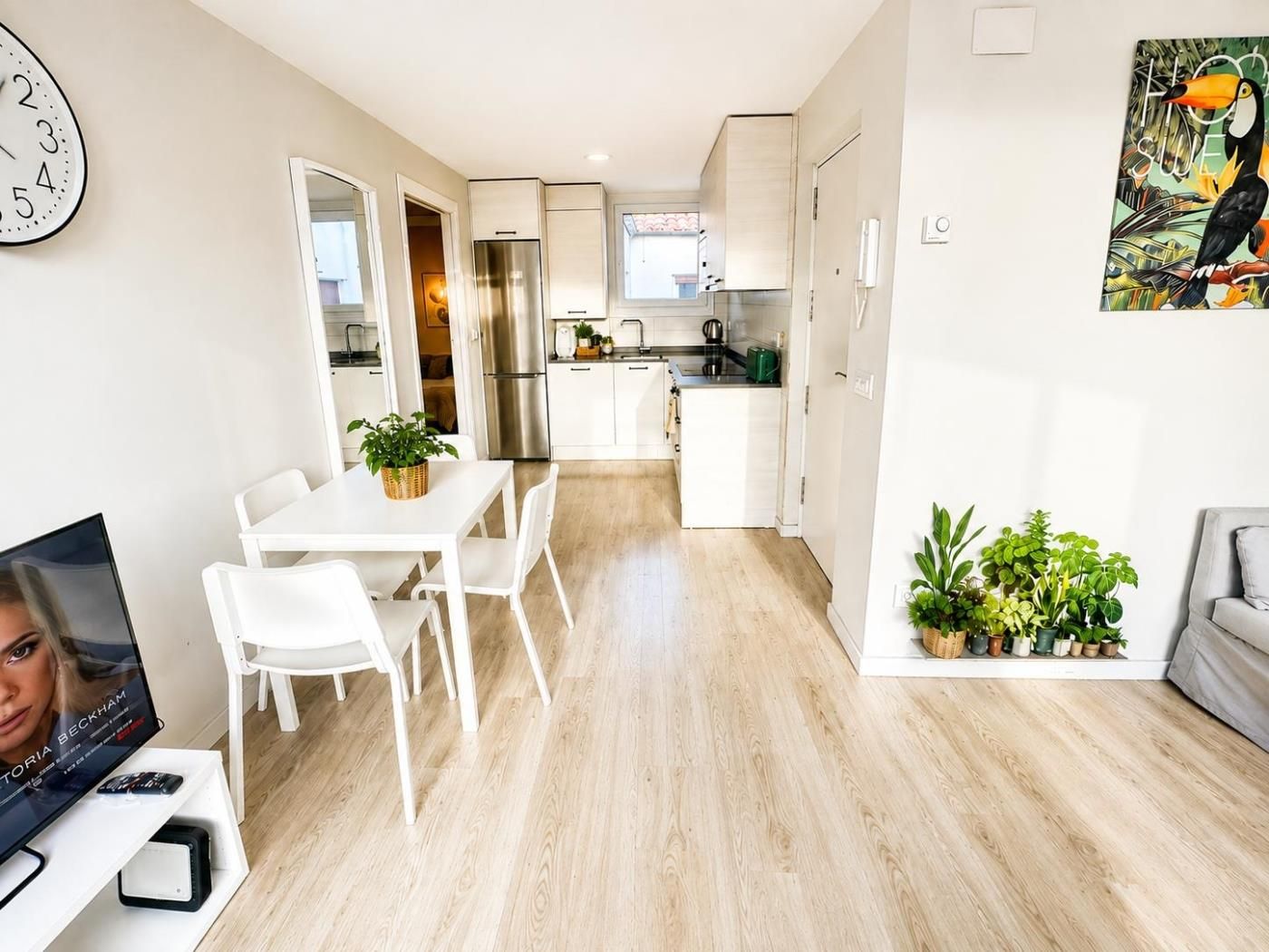 A modern kitchen with white cabinets, a stainless steel refrigerator, and a dining area with a white table and chairs.