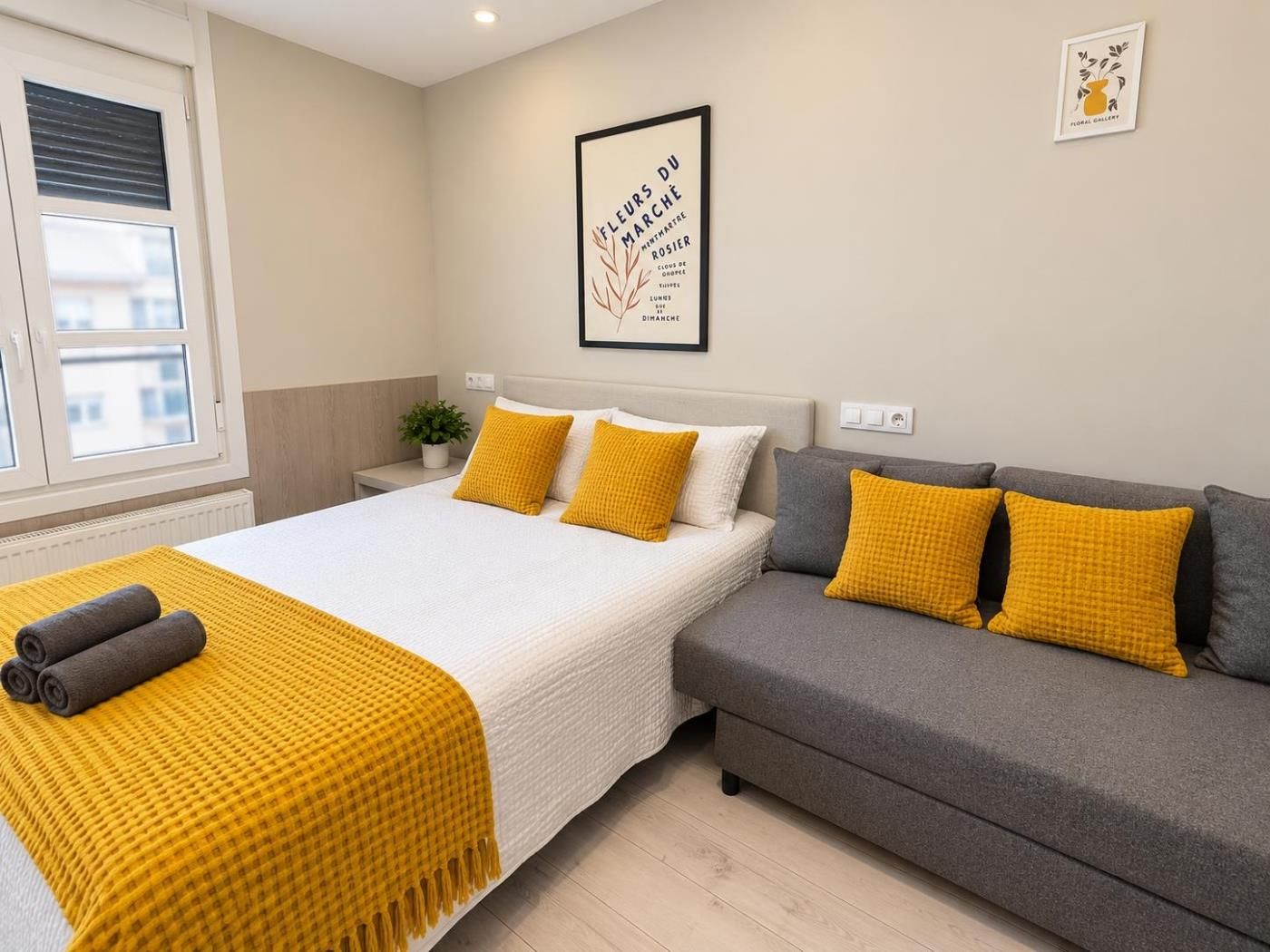 Een slaapkamer met een bed, een grijze bank en een gele plaid.