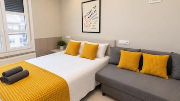 Un dormitorio con una cama, un sofá gris y una manta amarilla.