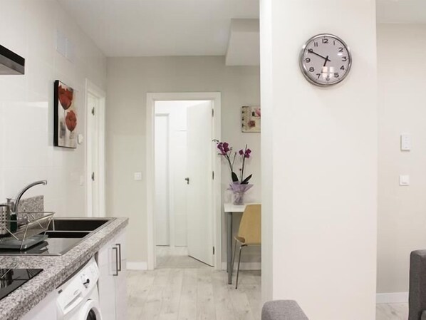 A modern kitchen with a built-in stove, a sink, and a countertop. There is a door leading to another room, and a clock on the wall. - APARTAMENTOS LOGROÑO CENTRO (LOGROÑO)
