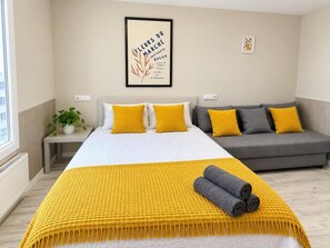 A hotel room with a bed, a sofa, a framed picture on the wall, and a potted plant. - APARTAMENTOS LOGROÑO CENTRO (LOGROÑO)