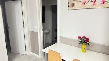 Una habitación con una mesa blanca, dos sillas, un jarrón con flores y un adorno en la pared.