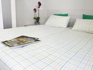 A bed with a checkered bedspread, a magazine on the bed, and a small potted plant with flowers. - APARTAMENTOS LOGROÑO CENTRO (LOGROÑO)