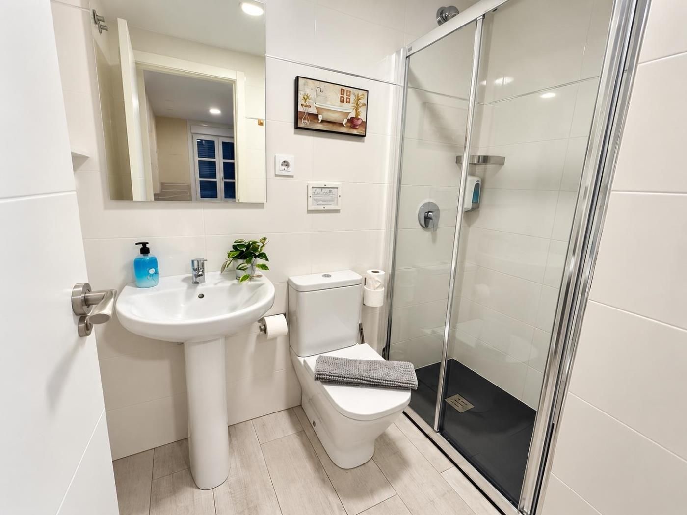 Un baño moderno con lavamanos blanco, inodoro y ducha con cerramiento de vidrio.