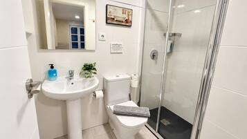 Un baño moderno con lavamanos blanco, inodoro y ducha con cerramiento de vidrio.