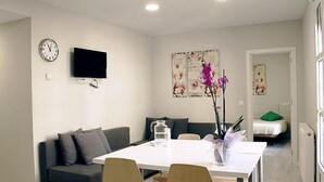 A modern living room with a sofa, a dining table, chairs, a flat-screen TV, artwork on the wall, and a door leading to another room. - APARTAMENTOS LOGROÑO CENTRO (LOGROÑO)