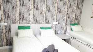 A double bed with white bedding and green pillows, a small bedside table, and a wooden wall paneling. - APARTAMENTOS LOGROÑO CENTRO (LOGROÑO)