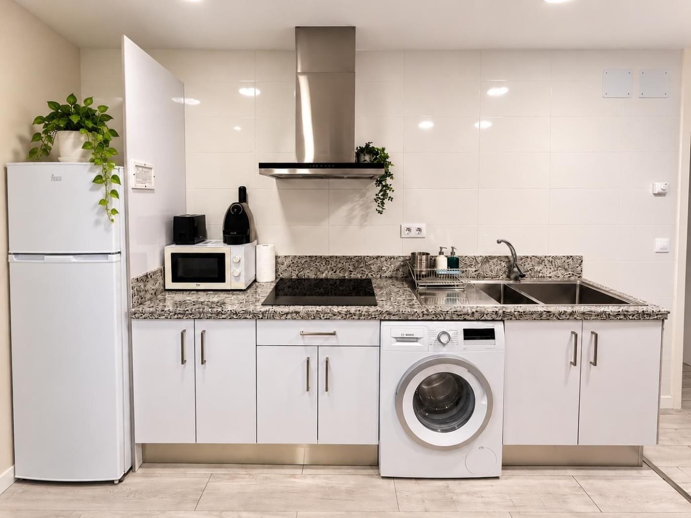 A modern kitchen with a built-in dishwasher, a microwave, a sink, and a stainless steel range hood.