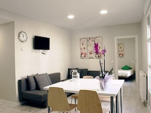 A modern living room with a sofa, a dining table, chairs, a flat-screen TV, artwork on the wall, and a door leading to another room. - APARTAMENTOS LOGROÑO CENTRO (LOGROÑO)