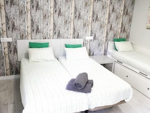 A double bed with white bedding and green pillows, a small bedside table, and a wooden wall paneling. - APARTAMENTOS LOGROÑO CENTRO (LOGROÑO)