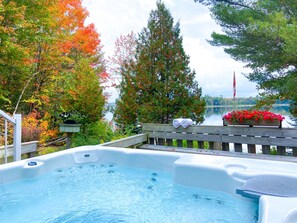 A hot tub with a wooden deck, surrounded by trees and a lake view. - 230' Lakefront, Hot Tub, Canoe/SUP, Fire, Dog OK (Baysville)