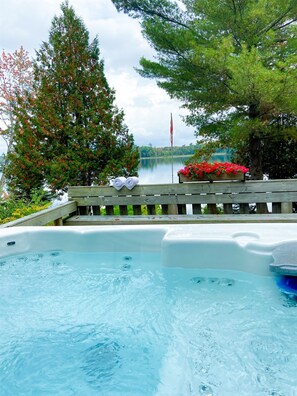 A hot tub with a view of a lake, surrounded by trees and a wooden deck. - 230' Lakefront, Hot Tub, Canoe/SUP, Fire, Dog OK (Baysville)