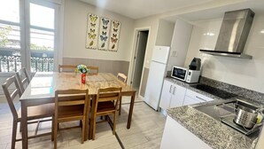A compact kitchen with a dining table, chairs, a microwave, and a stainless steel range hood. - APARTAMENTOS LOGROÑO CENTRO (LOGROÑO)