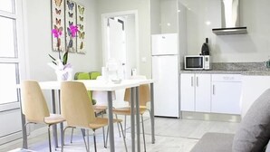 A modern kitchen with white cabinets, a microwave, and a stove. There is a dining area with a table and chairs. - APARTAMENTOS LOGROÑO CENTRO (LOGROÑO)