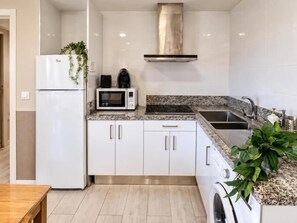 A modern kitchen with white cabinets, a stainless steel range hood, a microwave, and a washing machine. - APARTAMENTOS LOGROÑO CENTRO (LOGROÑO)