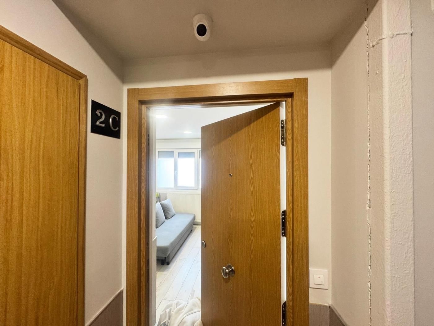 A hallway with a wooden door labeled '2C' leading to a room with a bed and a window.