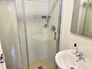 Une salle de bain moderne avec une douche à parois de verre, un lavabo doté d’un distributeur de savon et un miroir.