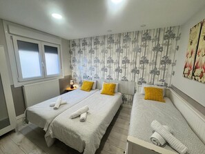 Une chambre d’hôtel avec deux lits, un radiateur, une fenêtre et un mur à rayures verticales.