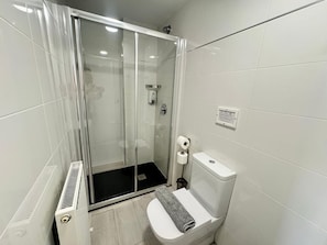 Un bany modern amb un plat de dutxa de vidre, un vàter i un assecador de mans.