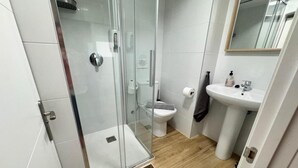 Et moderne badeværelse med brusekabine i glas, toilet og et spejl over vasken.