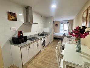 A compact kitchen with a washing machine, a microwave, and a sink. - APARTAMENTOS SAN NICOLAS (LOGROÑO)