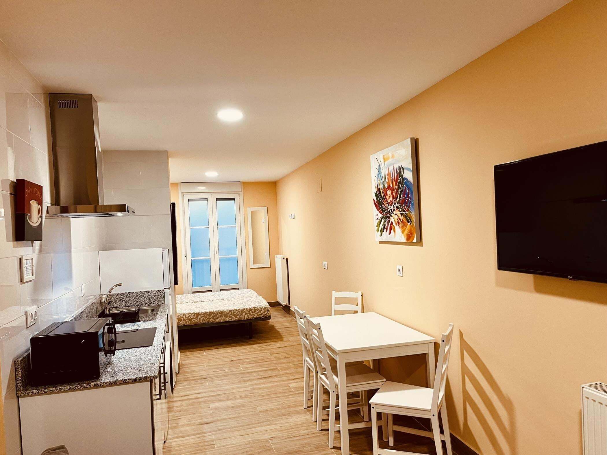 A compact kitchen with a microwave, toaster, and a white dining table with chairs.
