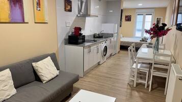 Un espacio habitable compacto con kitchenette, un sofá, una mesa de comedor y vistas al exterior.