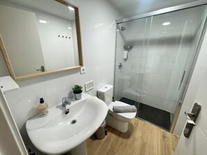 Casa de banho com lavatório branco, espelho, sanita e cabine de duche em vidro.