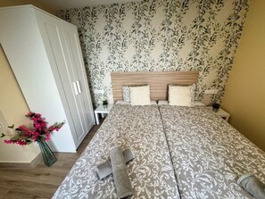 Quarto com cama de casal, guarda-roupa, mesa de cabeceira, um vaso com flores e parede com padrão.