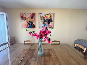A dining table with chairs, a vase with flowers, and two abstract paintings on the wall. - APARTAMENTOS SAN NICOLAS (LOGROÑO)