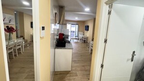 A hallway leading to a kitchen with a dining area, a TV mounted on the wall, and a door on the right. - APARTAMENTOS SAN NICOLAS (LOGROÑO)
