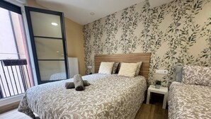 A bedroom with a bed, a nightstand, a potted plant, and a window with a view. - APARTAMENTOS SAN NICOLAS (LOGROÑO)