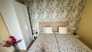 Ein Schlafzimmer mit einem Doppelbett, einem Kleiderschrank, einem Nachttisch, einer Vase mit Blumen und einer Wand mit Muster.