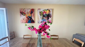 Ein Esstisch mit Stühlen, eine Vase mit Blumen und zwei abstrakte Gemälde an der Wand.