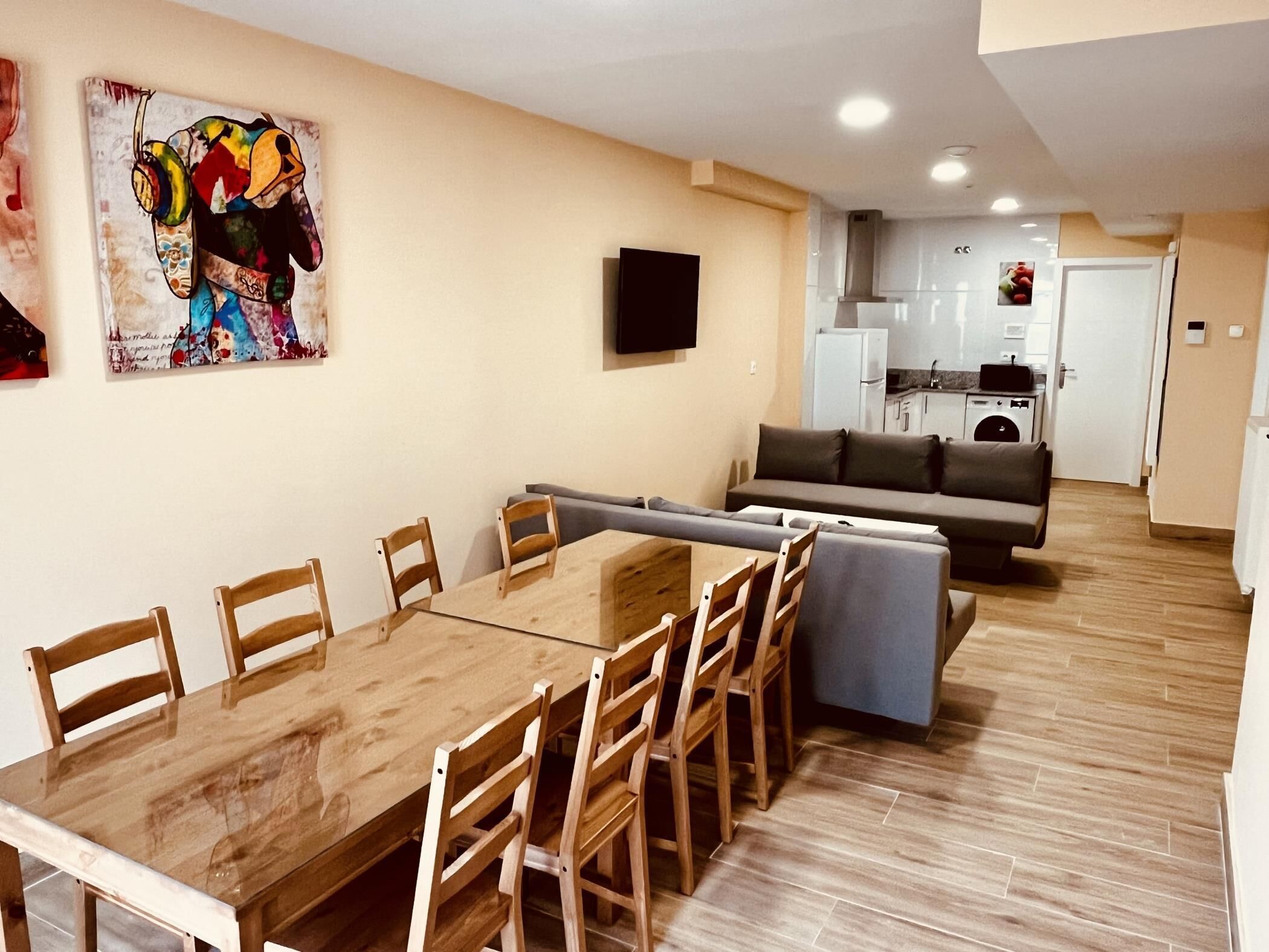 A dining area with a wooden table and chairs, a sofa, and a kitchen in the background.