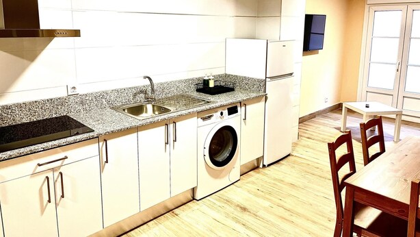 A compact kitchen with a washing machine, a sink, and a dining area with chairs. - APARTAMENTOS SAN NICOLAS (LOGROÑO)
