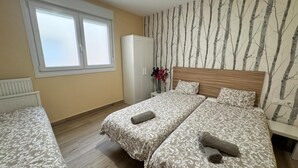 A bedroom with two beds, a window, a radiator, a wardrobe, and a wall with a tree pattern. - APARTAMENTOS SAN NICOLAS (LOGROÑO)