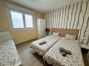 A bedroom with two beds, a window, a radiator, a wardrobe, and a wall with a tree pattern. - APARTAMENTOS SAN NICOLAS (LOGROÑO)