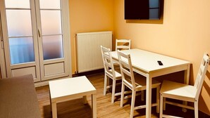 A room with a white table and chairs, a radiator, a TV mounted on the wall, and a sliding glass door. - APARTAMENTOS SAN NICOLAS (LOGROÑO)