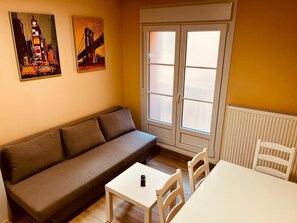 A room with a sofa, a small table, two chairs, a radiator, and two paintings on the wall. - APARTAMENTOS SAN NICOLAS (LOGROÑO)