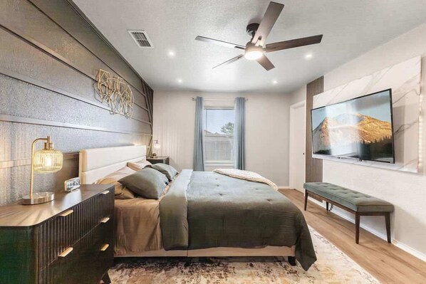A modern bedroom with a bed, bedside table, lamp, ceiling fan, TV, and a window with curtains. - Omni Smart House w/Alexa Voice Control Retreat (Killeen)