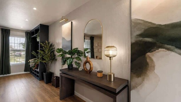 Un soggiorno moderno con pavimento in legno, un tavolino consolle scuro, uno specchio grande e un quadro appeso al muro.