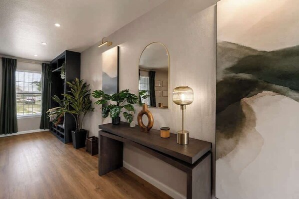 Un salon moderne avec un plancher en bois, une console sombre, un grand miroir et un tableau accroché au mur.