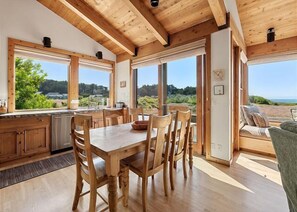 Ein Holzinterieur mit Esstisch und Stühlen, großen Fenstern und Blick ins Freie.