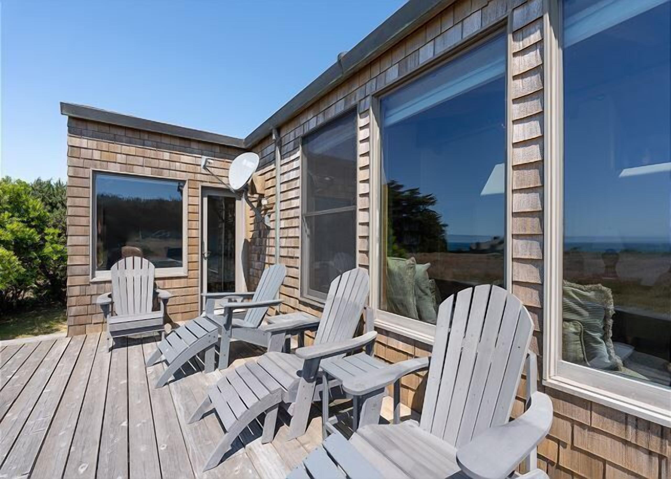 A wooden deck with Adirondack chairs, a satellite dish, and large windows.