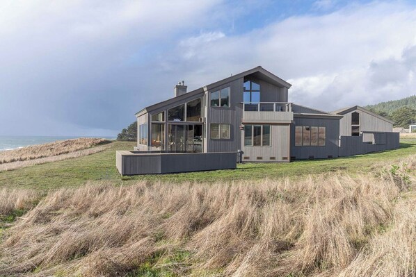 Une maison moderne à deux étages, dotée de grandes fenêtres, d’un balcon et offrant une vue sur l’océan.